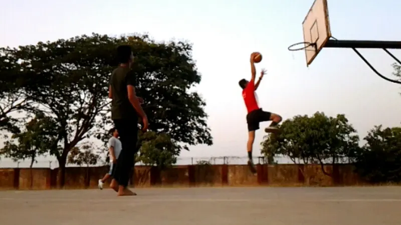 Basketball player jumping towards an outdoor hoop with the ball